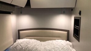 Una cama bien hecha con cabecera, repisa en la pared y lámpara colgante.