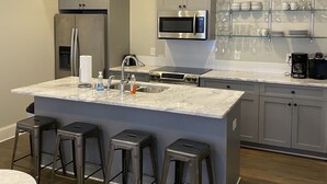 Una cocina moderna con una isla central, taburetes de bar, electrodomésticos de acero inoxidable y un estante de vidrio.