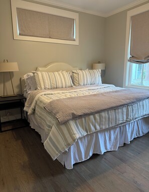 Uma cama bem arrumada com roupa de cama listrada, uma mesa de cabeceira com abajur e uma janela com vista para o exterior.
