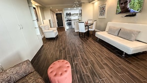 A modern living room with a white sofa, a pink ottoman, and a dining area with white chairs. - Pied-`a-Terre • Steps To Beach • Mangrove / Gulf View • Just Renovated (Naples)