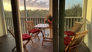 A balcony with a wooden table and chairs, a potted plant, and a view of trees and sky. - Pied-`a-Terre • Steps To Beach • Mangrove / Gulf View • Just Renovated (Naples)