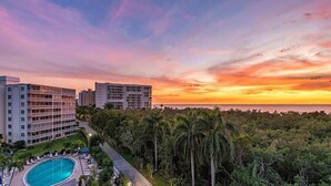A resort with a swimming pool, palm trees, and a view of the ocean at sunset. - Pied-`a-Terre • Steps To Beach • Mangrove / Gulf View • Just Renovated (Naples)