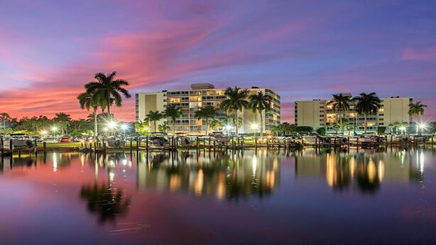 A waterfront hotel with multiple floors, palm trees, and a calm water body reflecting the lights. - Pied-`a-Terre • Steps To Beach • Mangrove / Gulf View • Just Renovated (Naples)