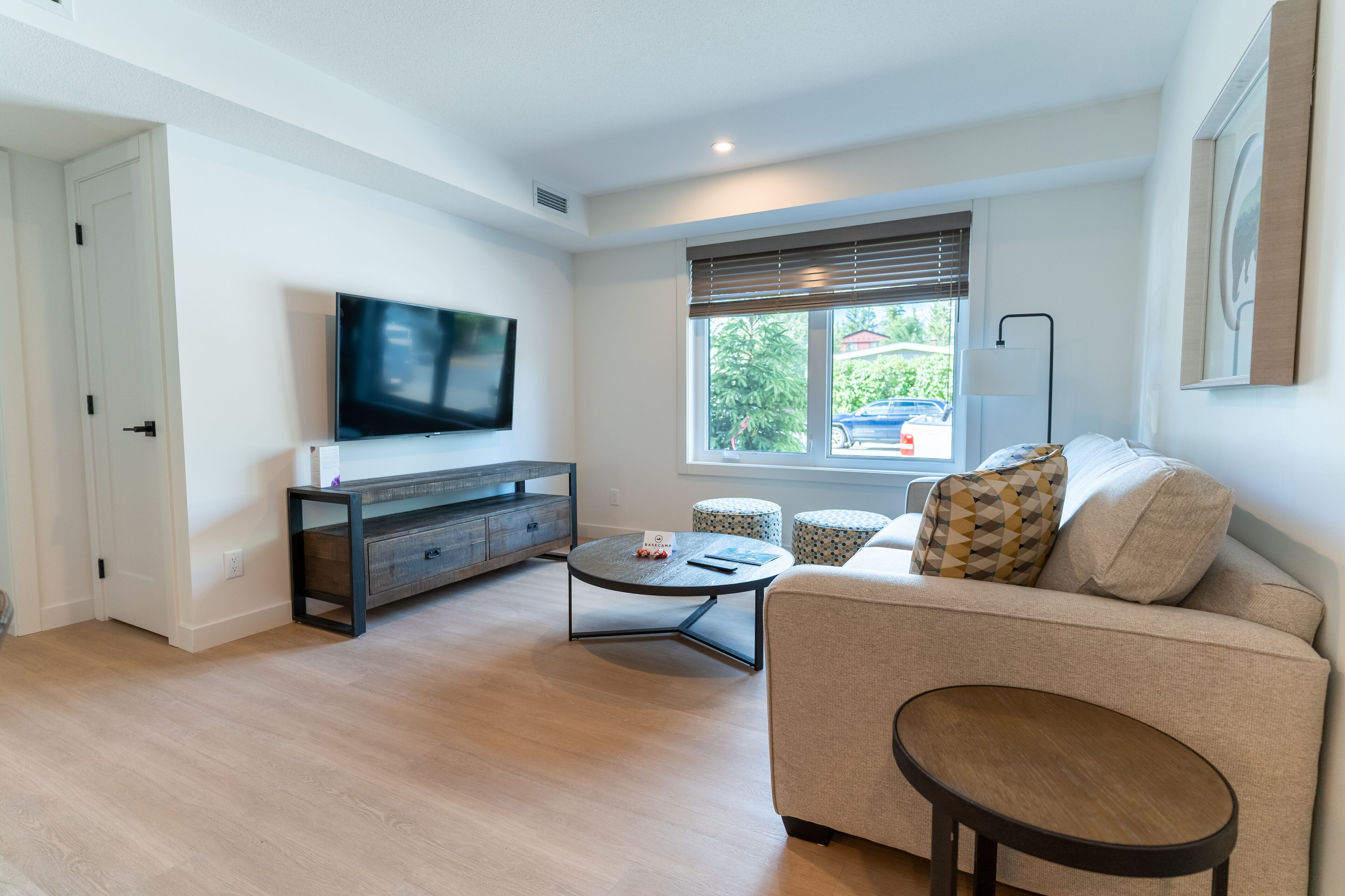 A modern living room with a flat-screen TV, a sofa, a coffee table, and a window with blinds.