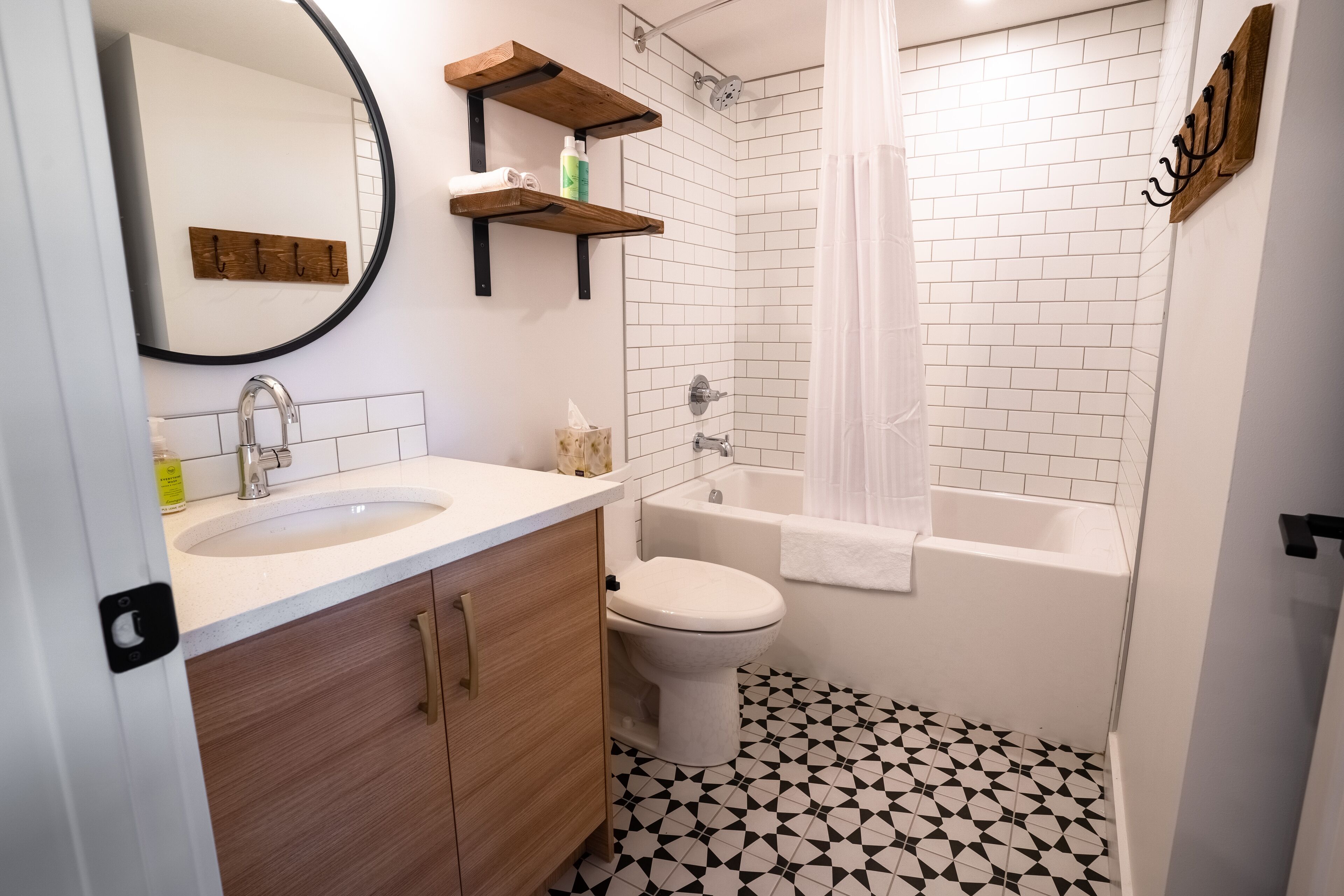 Une salle de bain avec un lavabo, des toilettes et une baignoire. Il y a des étagères en bois au-dessus du lavabo et un miroir sur le mur.