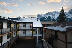 Um edifício com vários andares, um pátio coberto, uma escadaria e vista para montanhas nevadas ao fundo.