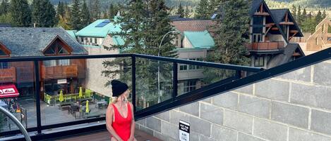 A woman sitting by a pool with a mountain view, a sign indicating hot tub depth, and a covered area with outdoor seating.