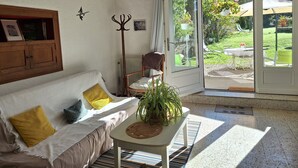A cozy room with a wooden ceiling, a white sofa with yellow and grey cushions, a small table with a plant, and a view of a garden through a glass door. - Estuvi - La Sittelle Enchantée, a break in the countryside. bike shelter, animals ok  (CHEMENOT)