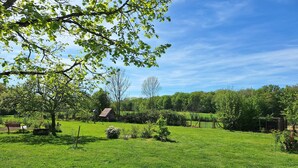 A lush green field with a small wooden structure, possibly a shed or barn, surrounded by trees and a clear sky. - Estuvi - La Sittelle Enchantée, a break in the countryside. bike shelter, animals ok  (CHEMENOT)