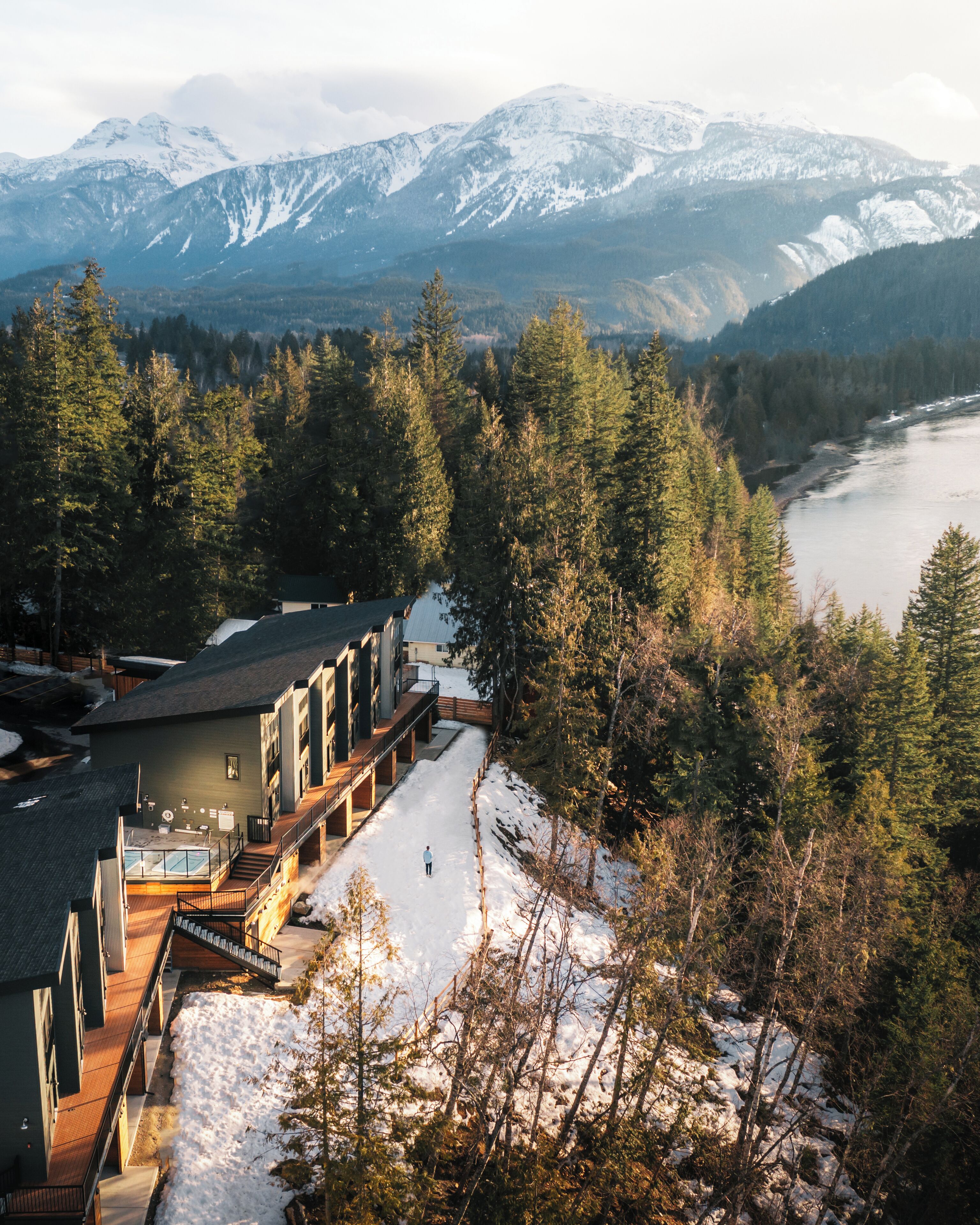 A modern building with a glass conservatory, a wooden deck, and a snow-covered landscape with mountains in the background.