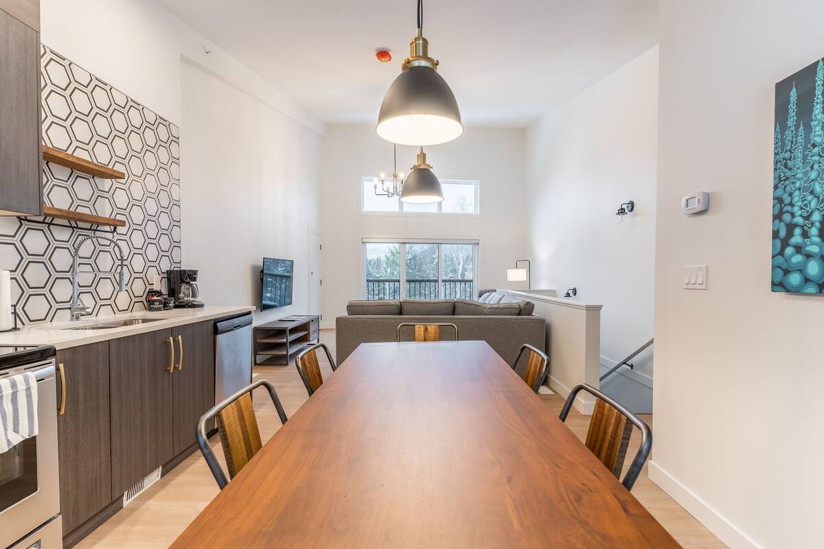 A modern kitchen with a wooden dining table, dark cabinets, and a hexagonal backsplash.