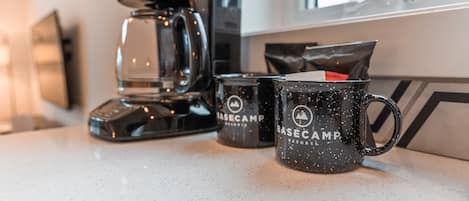 Una cafetera, dos tazas y un bolso sobre una encimera de cocina.