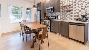 A modern kitchen with a wooden dining table, dark cabinets, and a geometric backsplash. - Basecamp Resorts Revelstoke (Revelstoke)
