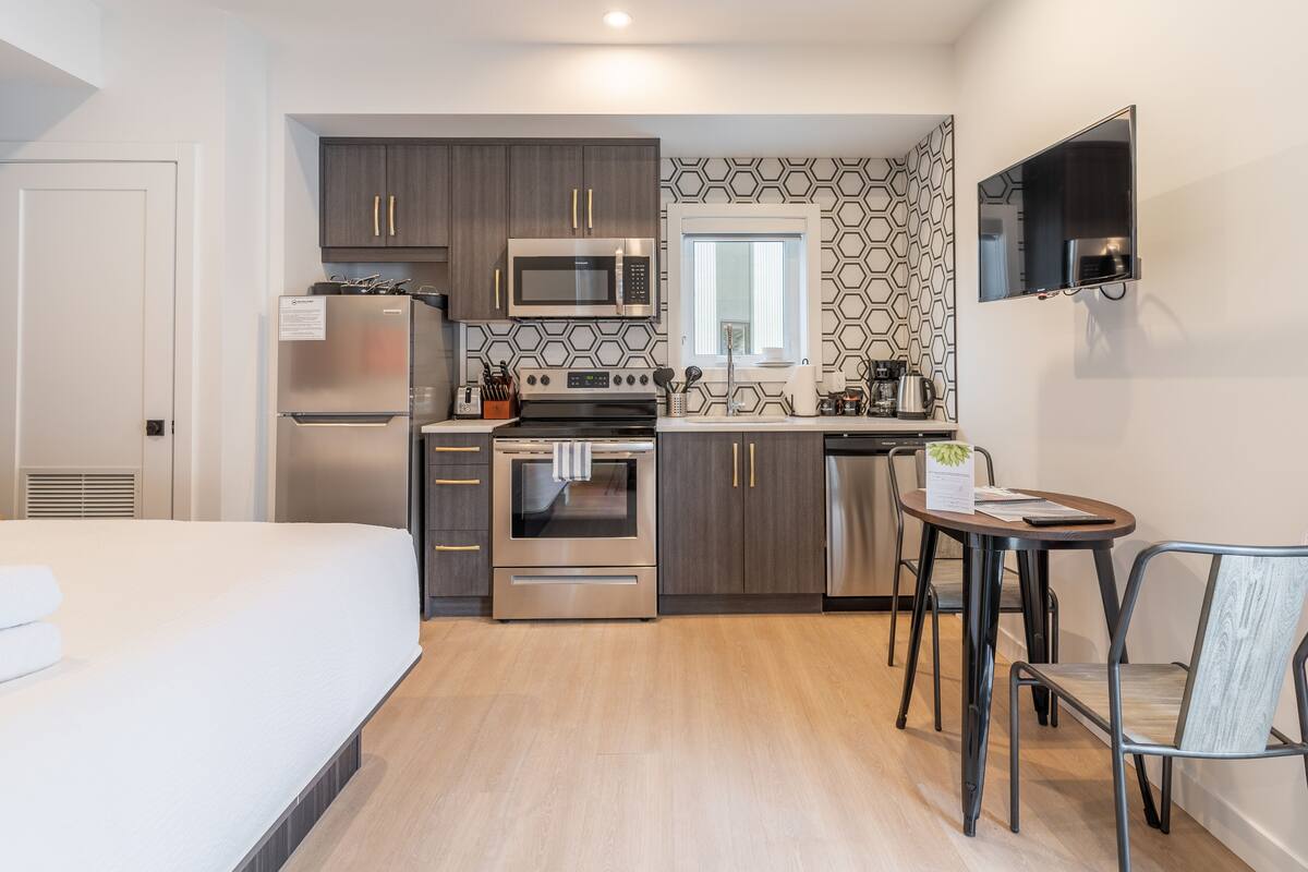 A compact hotel room with a kitchenette, a bed, and a small dining area.