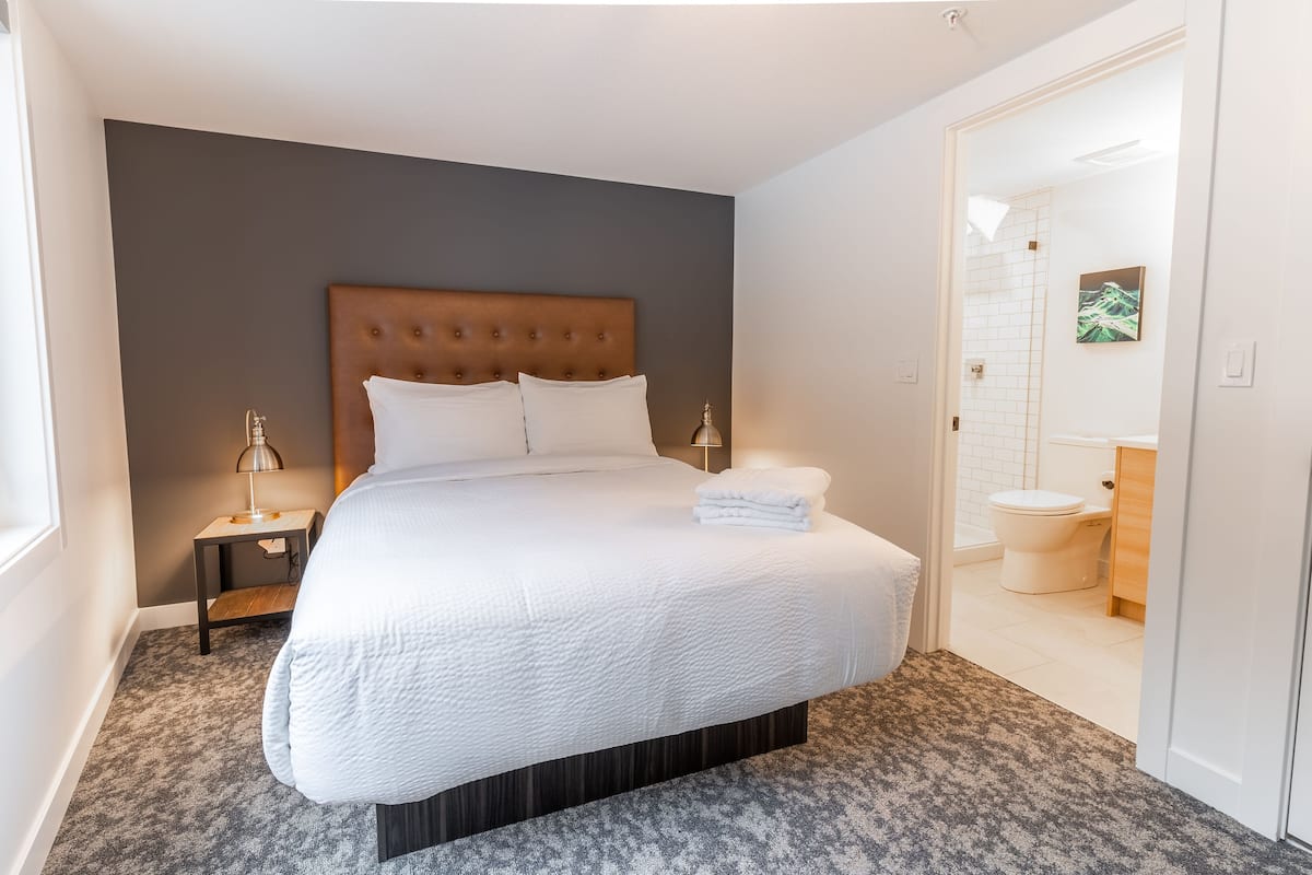 A neatly made bed with white linens, a wooden headboard, and a small bedside table with a lamp.