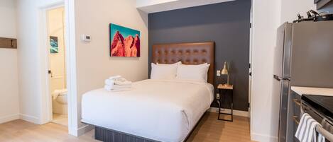 Habitació d'hotel moderna amb un llit gran, una petita taula de nit, un frigorífic i un quadre a la paret.
