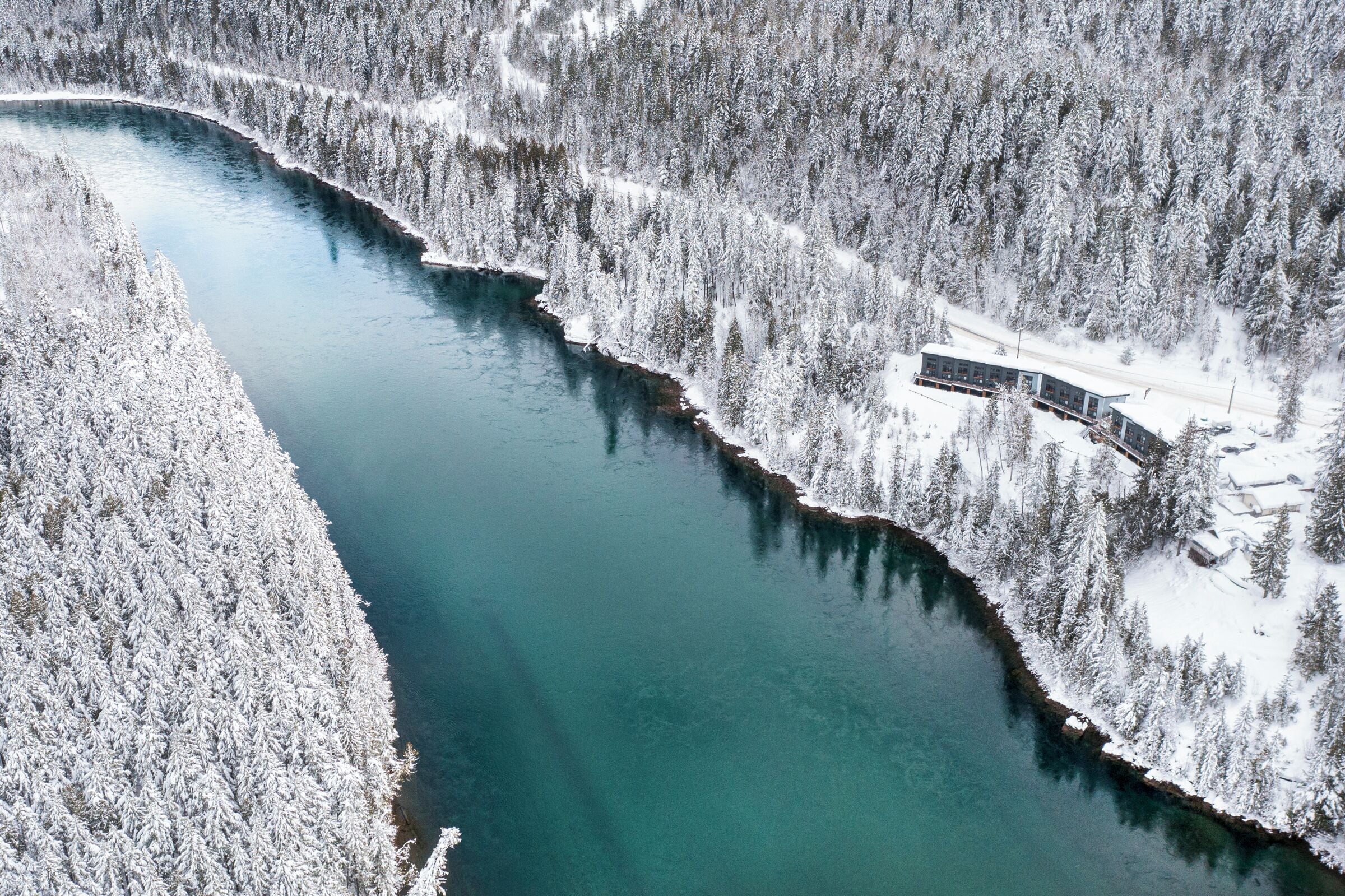 An aerial view of a snow-covered river with a building adjacent to it.