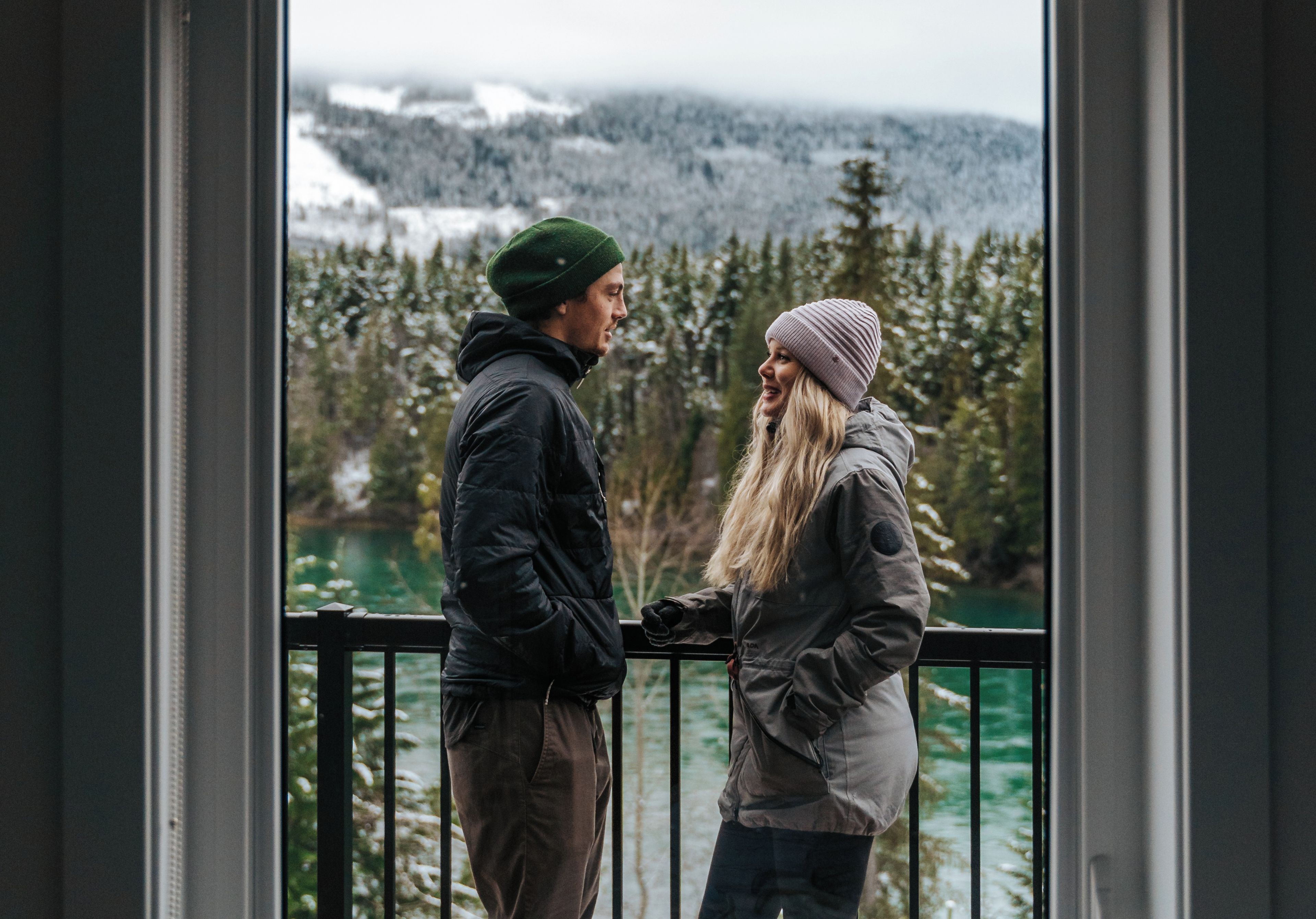 Dos personas de pie junto a una ventana con vistas a un bosque y un lago.