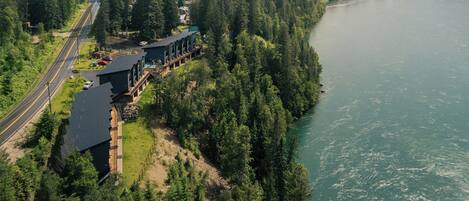 An aerial view of a lodge with a road leading to it, surrounded by dense forest and a river.
