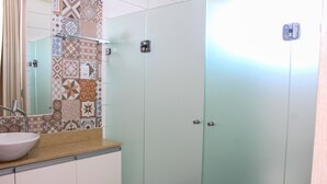 Une salle de bain avec un mur recouvert de carreaux derrière le lavabo, un lavabo et une porte dotée d’une poignée.