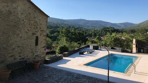 Ein Steinhaus mit Pool und Liegestühlen, umgeben von Grünflächen und Bergen.