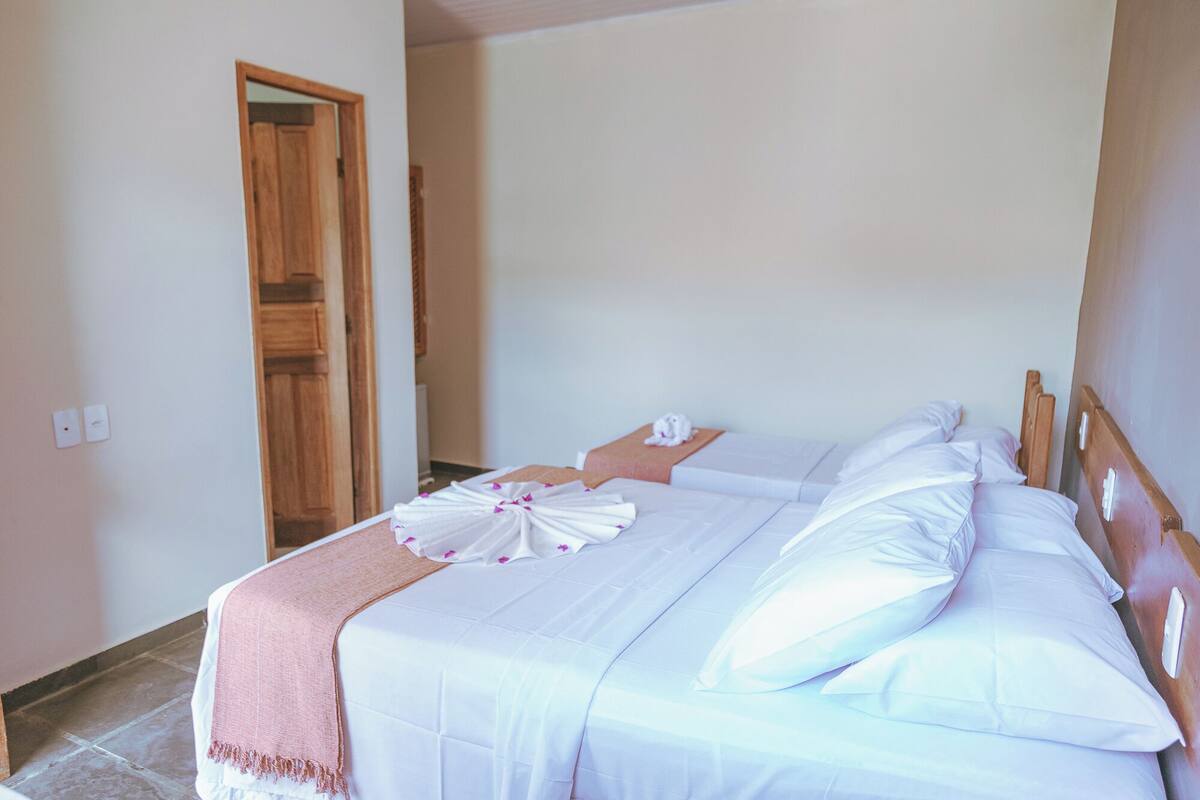 A hotel room with a bed, a wooden door, and a small table with a towel and a bottle.