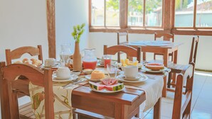 A wooden dining table set with plates, bowls, and glasses, with a window in the background. - Pousada Porto Da Barra (Porto Seguro)