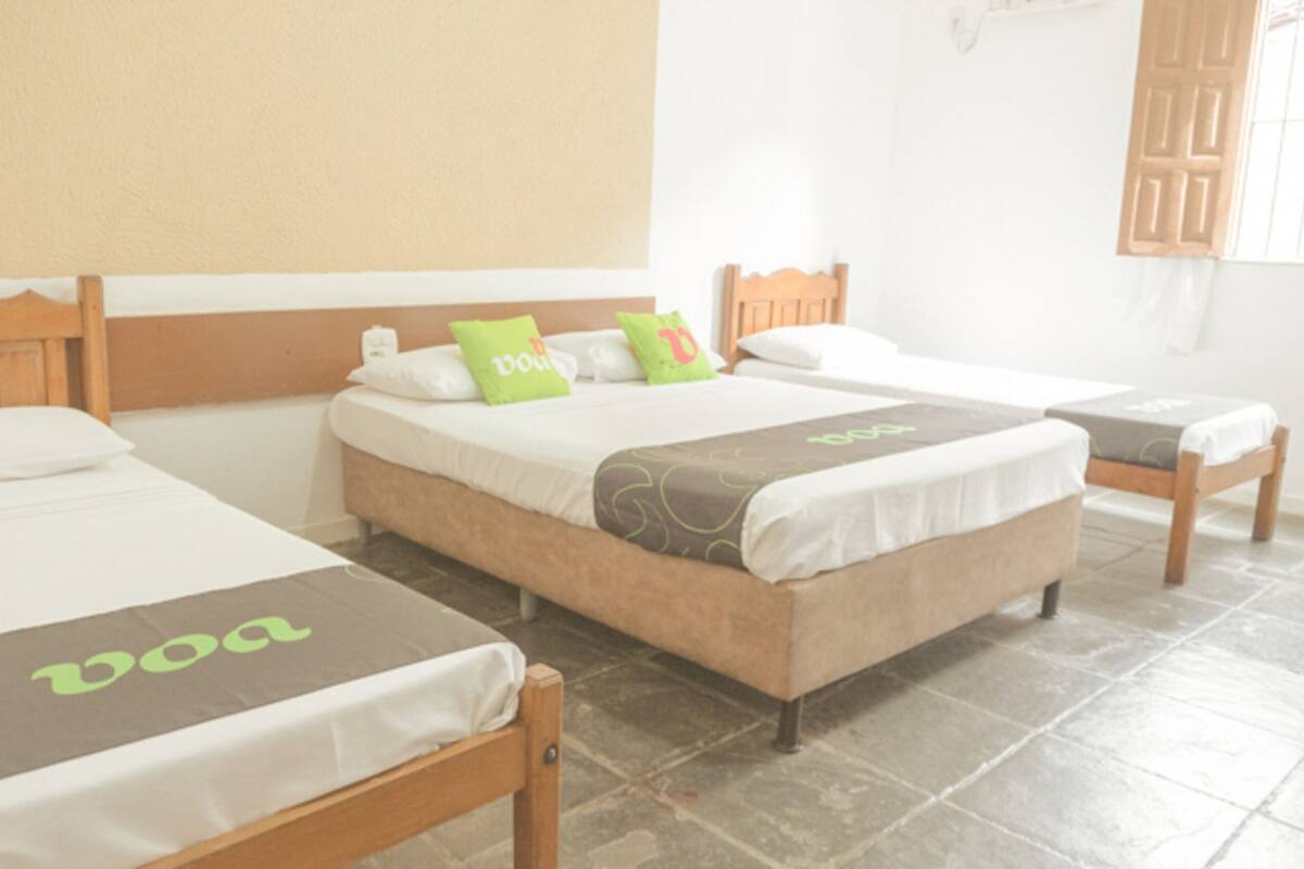 Three single beds with wooden headboards, white bedding, and green and brown decorative pillows.