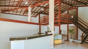 A spacious interior with a high ceiling, wooden beams, a central island counter, a staircase, and a cozy seating area. - Pousada Porto Da Barra (Porto Seguro)