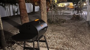 A barbecue grill on a patio with a white fence and trees in the background. - Gulf  Beach Bungalow (Holmes Beach)