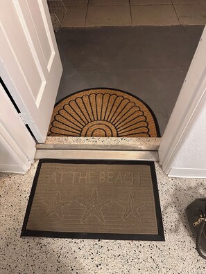 Une porte avec un paillasson et un tapis sur lequel est inscrit : « À LA PLAGE ».
