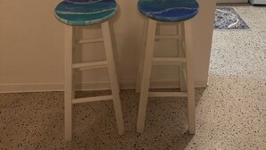 A kitchen with white cabinets, a coffee maker, and two stools with blue-tinted tops. - Gulf  Beach Bungalow (Holmes Beach)