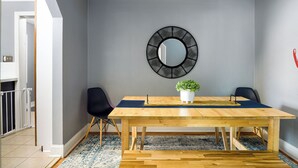 A dining area with a wooden table, two chairs, a potted plant, and a wall-mounted mirror. - Market 6min, HPU 2Min, Private Patio, Downtown 5min, Dogs Ok, 3 SMART TVs (High Point)