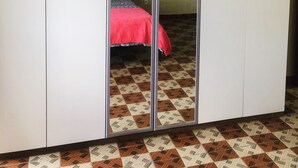 Ein Zimmer mit Schrank, Bett mit roter Decke und gemusterten Bodenfliesen.