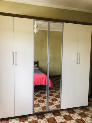 Una stanza con un armadio, un letto con coperta rossa e piastrelle del pavimento a motivi.