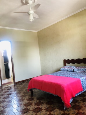 Quarto com cama, ventilador de teto e piso estampado.
