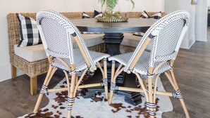 Un coin repas avec une table en bois, deux chaises en osier, un tapis en peau de vache et un lustre suspendu.