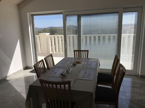 Un coin repas avec une table dressée pour six personnes, de grandes fenêtres et une vue sur l’extérieur.