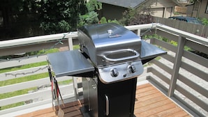 Ein tragbarer Gasgrill auf einer Holzterrasse mit weißer Geländer.