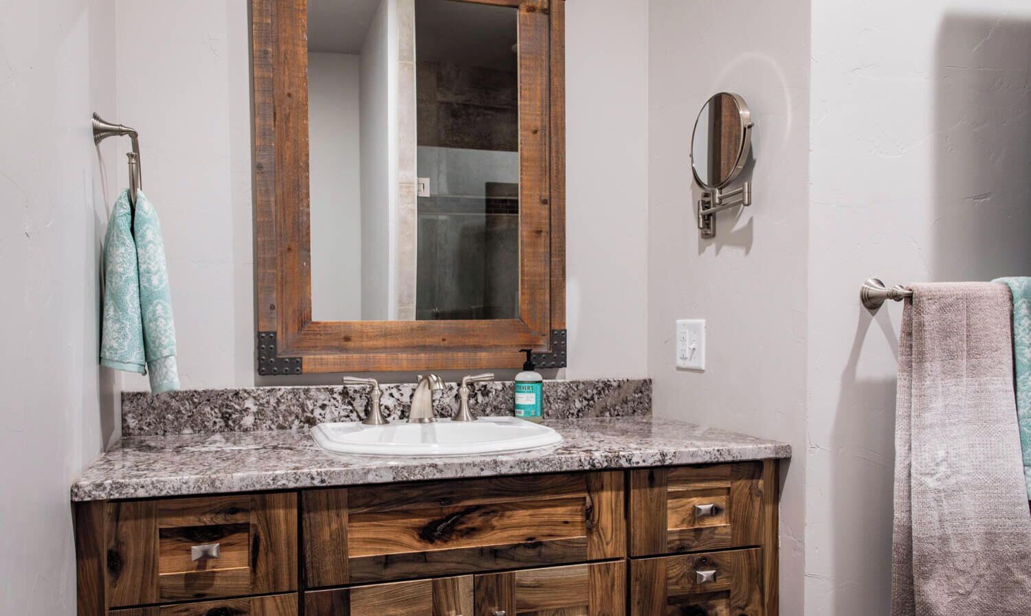 A bathroom with a granite countertop sink, wooden vanity, a large mirror, and two towels hanging on towel bars.