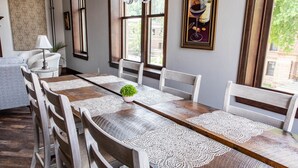 Un comedor con una larga mesa de madera, sillas blancas y copitos de encaje. Hay una pequeña planta en maceta sobre la mesa.