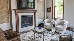 Una sala de estar con chimenea, televisor montado arriba, dos sillones, una mesa de centro y papel tapiz estampado.
