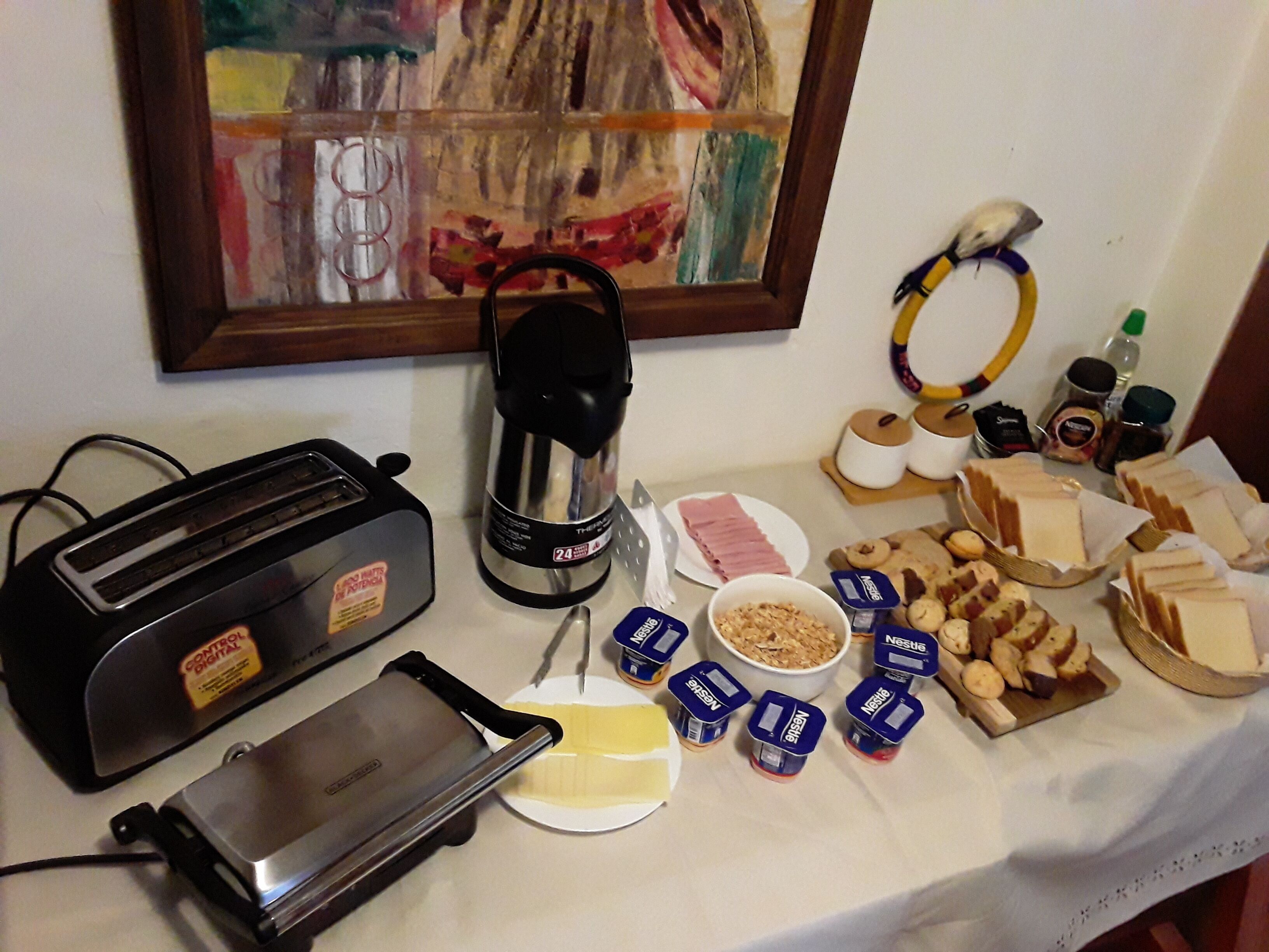 A breakfast table with a toaster, coffee maker, plates of food, and various condiments.