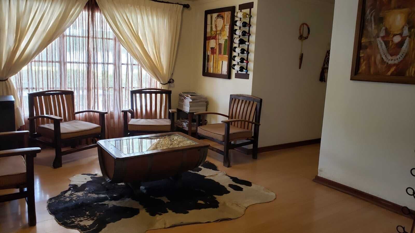 Una sala de estar con una mesa de centro de vidrio, sillas de madera, un tapiz de cuero de vaca y una estantería para vinos en la pared.