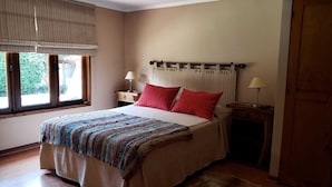 A bedroom with a bed, a bedside table with a lamp, a window with curtains, and a door. - Tierra y Vino (Santa Cruz)