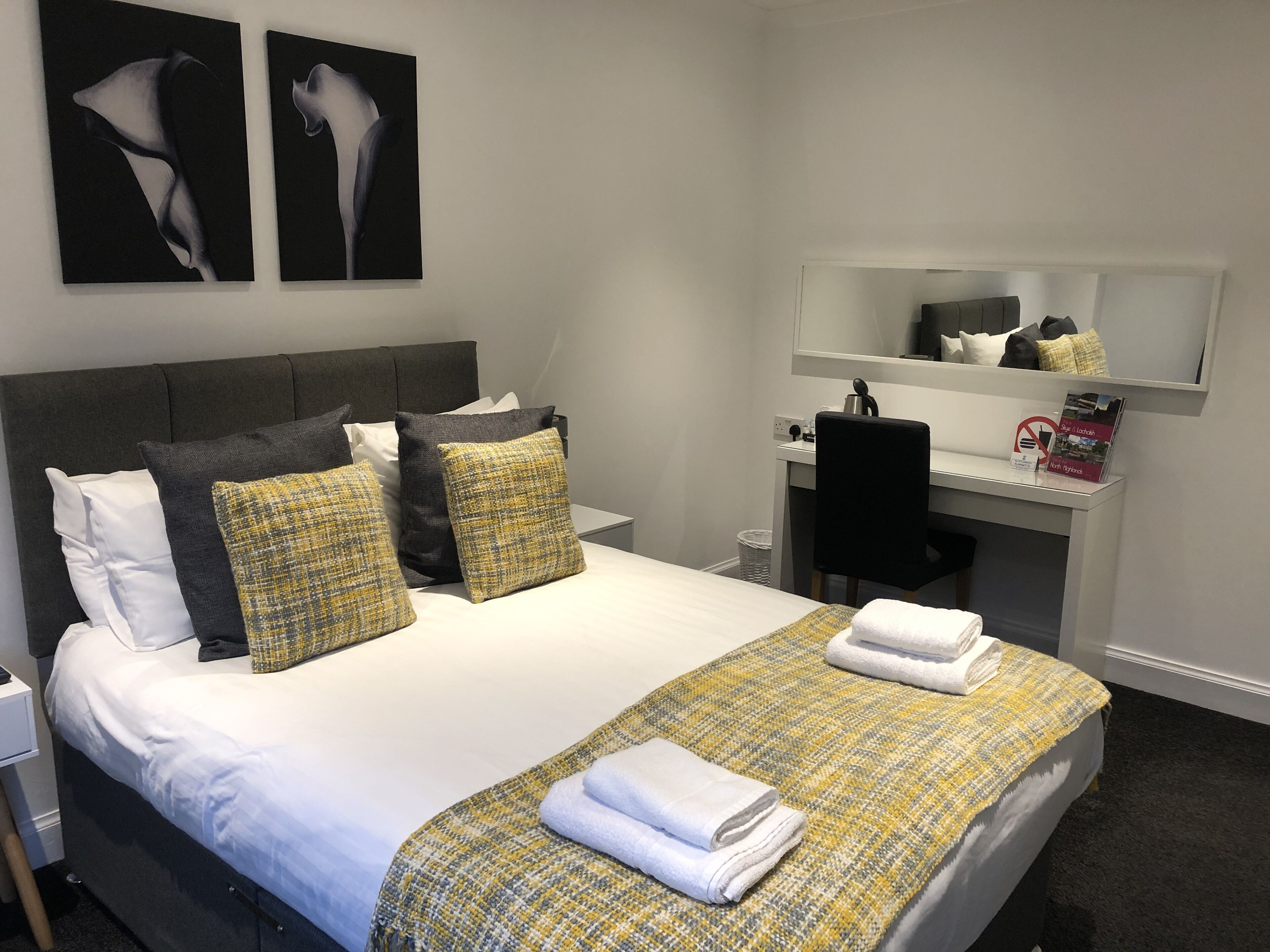 A hotel room with a bed, a desk, and a mirror.
