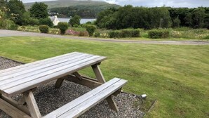 A wooden picnic table in a grassy area with a view of a lake and hills in the background. - Glendaruel Bed & Breakfast (Portree)