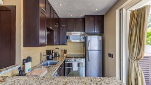 A kitchen with dark cabinets, a granite countertop, a microwave, a refrigerator, and a stove.