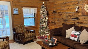 Un salon chaleureux avec un plafond en bois, un sapin de Noël, un canapé marron et une table basse en bois.