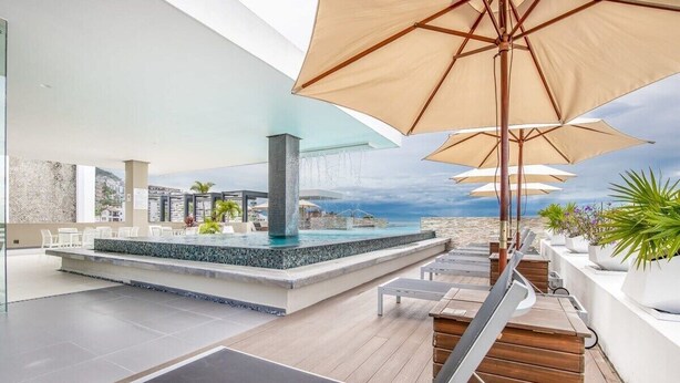 Een dakzwembad met een jacuzzi, lounge stoelen en parasols.
